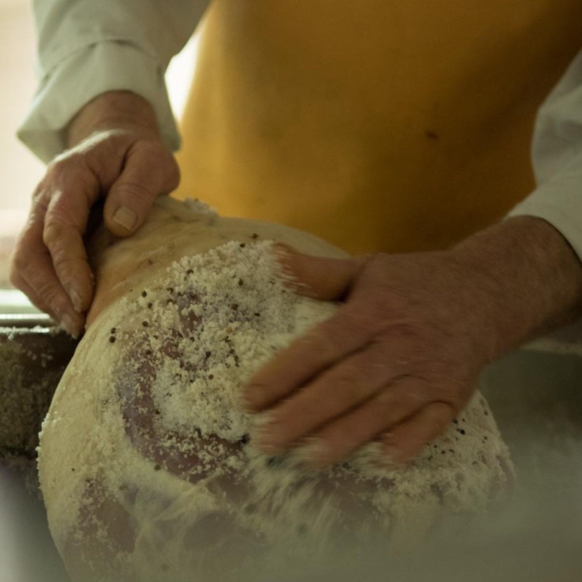 Hand reibt Schinken mit Salz ein